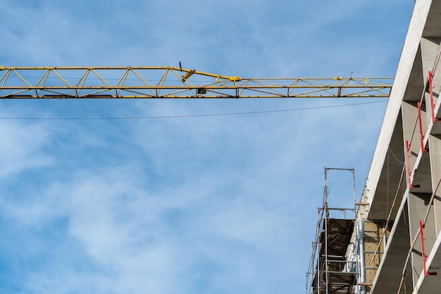 Construction site A residential building under construction A large tower crane is working on a building under construction Crane boom on a background of blue sky and white clouds