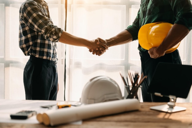 Construction team shake hands greeting start new project plan behind yellow helmet on desk in office center to consults about their building projectxAxA