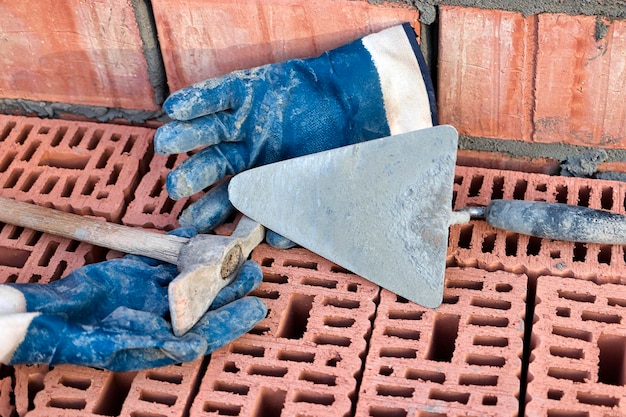 Строительный шпатель для укладки кирпича и блоков Строительный инструмент каменщика Ручной рабочий инструмент на фоне кирпичной кладки