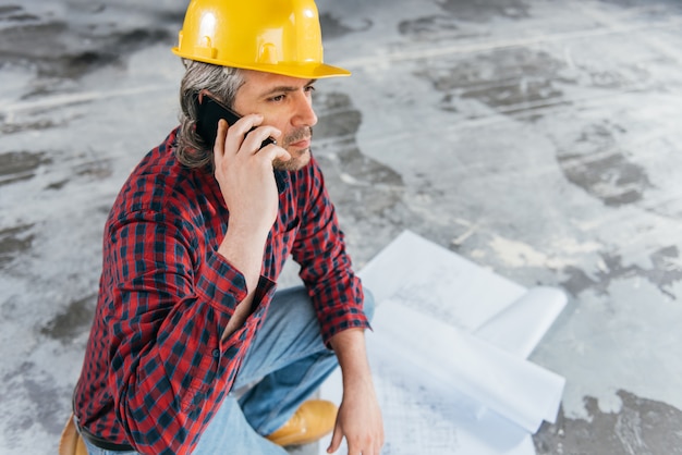 Photo construction worker checking blue prints and talking on the phone