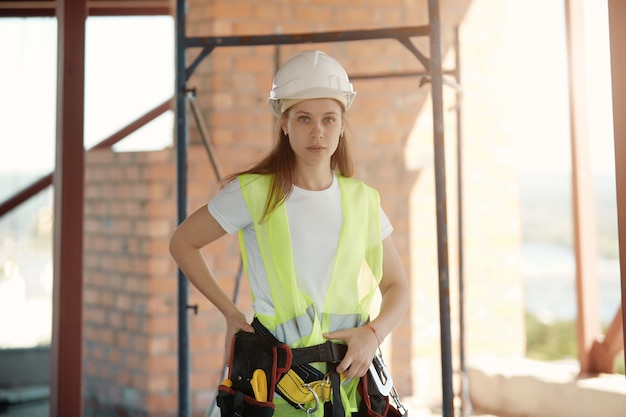 Construction worker girl with a seat belt and tool bag on the  of a construction site