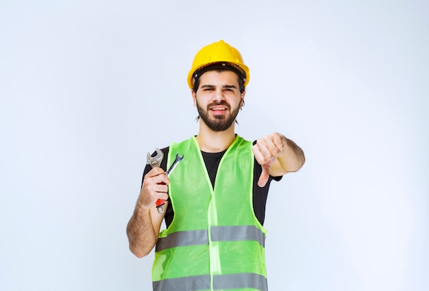 Construction worker holding wrench and spanner and showing dislike sign.