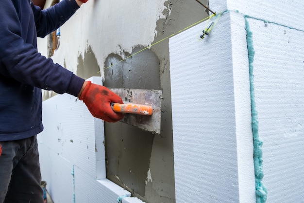 Construction worker installing styrofoam insulation sheets on house facade wall for thermal protection.