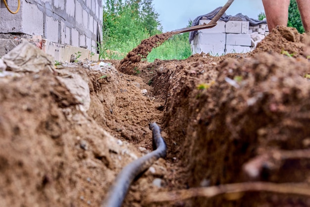 Construction worker is digging trench for laying cables using shovel to excavate soil