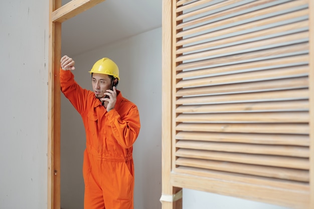 Photo construction worker leaning on door frame and talking on phone with coworker or family member