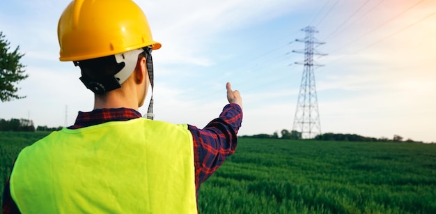 Construction worker pointing to the electricity pylon Electrician wearing yellow hard hat waistcoat