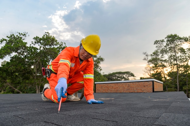 Construction worker putting the asphalt roofing (shingles) with nail gun on a large commercial apartment building development