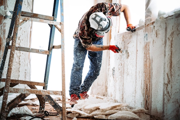 Construction worker removing spray foam on the walls of a building