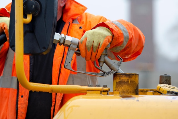 Construction worker in safety gloovs filling excavator with diesel fuel on construction site