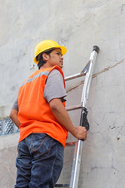 Photo construction worker in safety helmet and vest standing on stepladder checking wires at construction