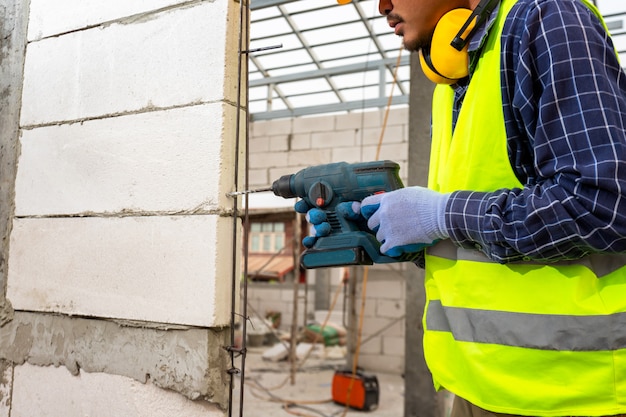 Construction worker use a drill bit,Engineer wearing safety equipment (helmet and jacket) uses a power drill to mount a aerated brick wall.