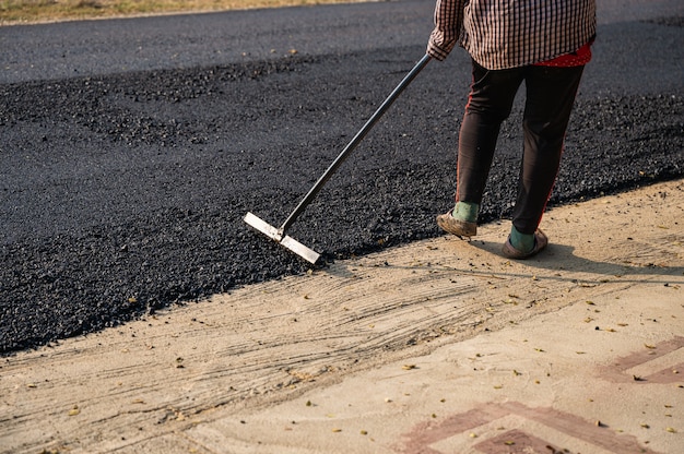 도구를 사용하는 건설 노동자는 손상된 고속도로에서 핫 믹스 아스팔트 도로를 정확하게 수평으로 퍼뜨립니다.
