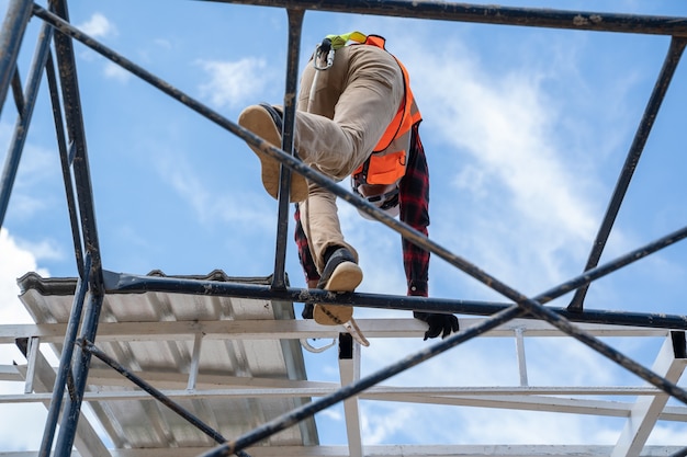 Construction worker wearing safety harness and safety line with\
tools are climbing scaffolding working at height.