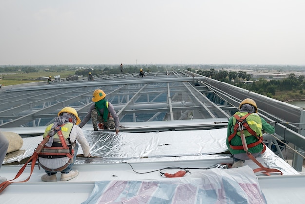 Construction worker wearing safety harness and safety line working on a metal industry roo