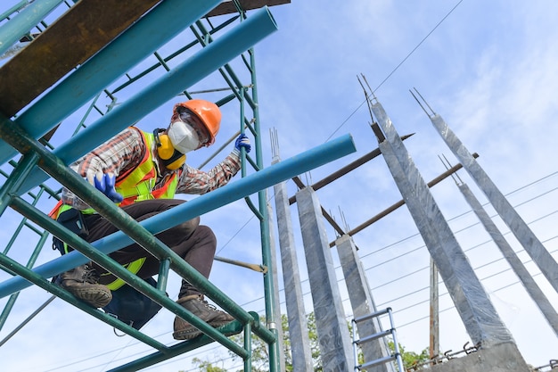 Operaio edile che indossa lavori di sicurezza in alta uniforme su impalcature in cantiere durante il tramonto, attrezzature di lavoro in altezza.