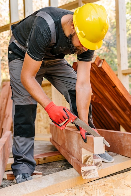 Foto operaio edile con cappello duro taglio pezzo di legno con sega