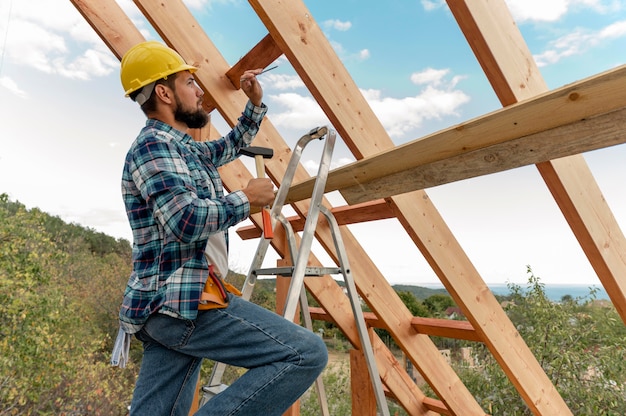 Photo construction worker with hard hat and hammer building the roof of the house