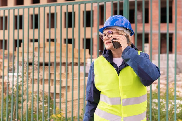 Construction worker woman on construction site in green vest and helmet with phone 