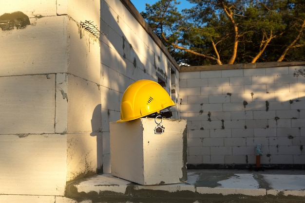 Строительная желтая каска и ключ от дома на окне жилого дома из блоков пористого бетона. Строительство под ключ, будущий дом, инженерия, постройка. Безопасность труда. Копировать пространство