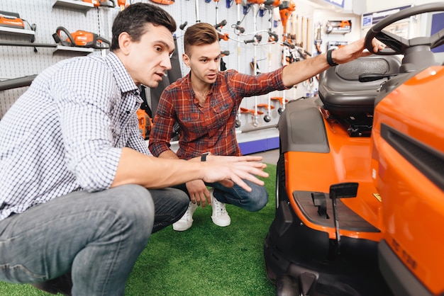 Photo consultant in garden tools store shows customer lawn mower.