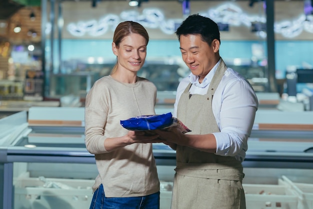 Consultant in a supermarket a friendly asian man in an apron offers a young beautiful woman to buy a