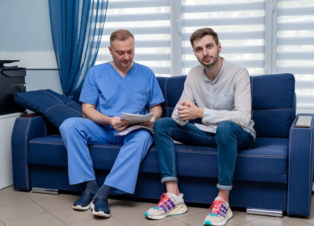 Consultation at clinic. Doctor and male patient sitting on sofa in office.