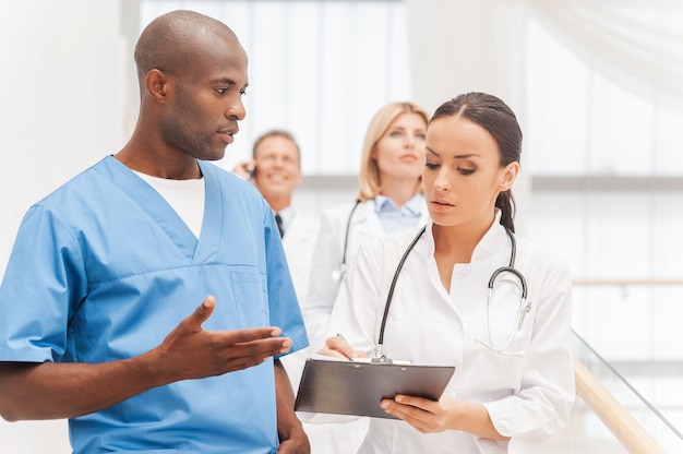 Consulting on the go. Group of confident doctors moving downstairs while two of them discussing something and gesturing