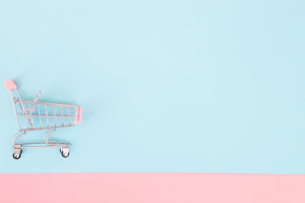 Потребительская концепция мини-тележка для покупок на цветном фоне минимализма вид сверху