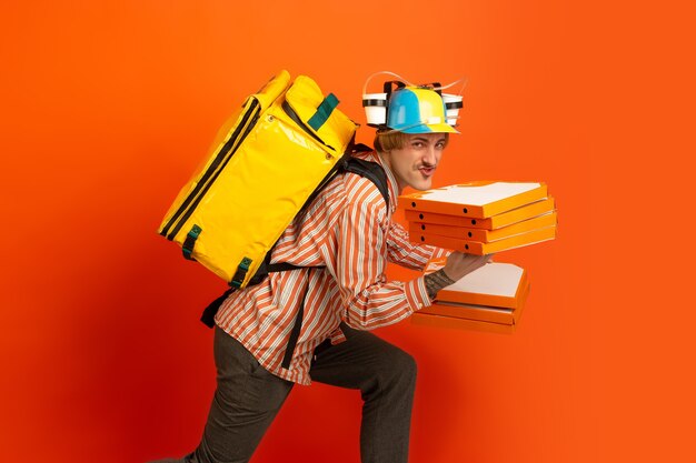 Contacless delivery service during quarantine. Man delivers food and shopping bags during insulation. Emotions of deliveryman isolated on orange background.