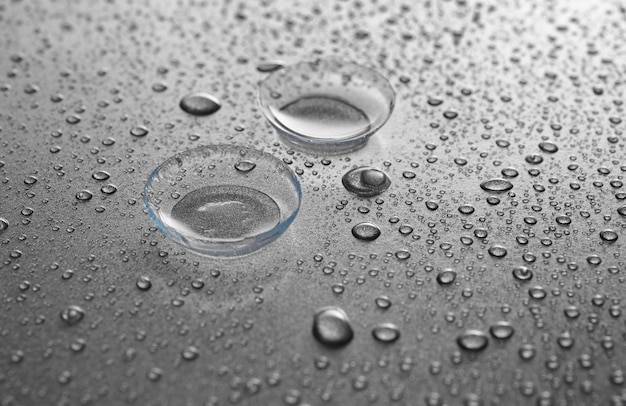 Contact lenses and drops of water on gray background