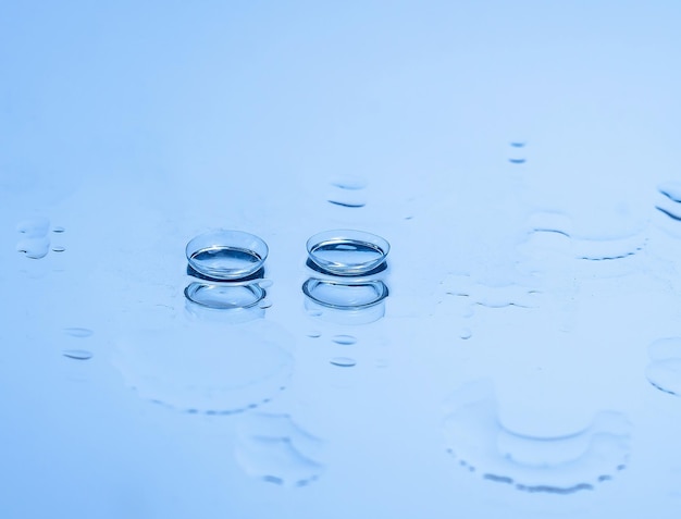 Contact lenses for the eyes on the glass among the drops of water in blue Optical equipment