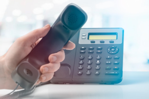 Contact us office voip phone with handset up on table with blurred office background Communication support call center and customer service help desk