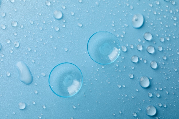 Contactlenzen op blauw oppervlak met waterdruppels, bovenaanzicht