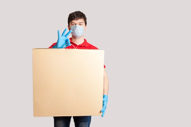 Consegna senza contatto. uomo di consegna maschio in uniforme, guanti di gomma e una maschera medica detiene una scatola. ordinazione online durante la quarantena del coronavirus.