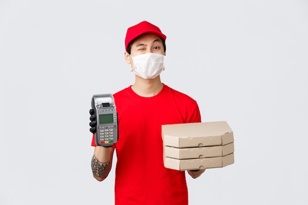 Contactless delivery, safe purchase and shopping during coronavirus concept. Cheerful fast-food employee or courier in red uniform cap, t-shirt, bring POS terminal with pizza to client, bring order.