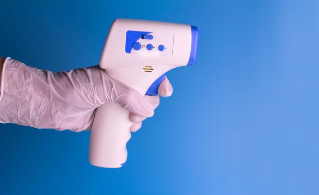 Contactless thermometer in the hand of a man in a medical glove on a light blue background