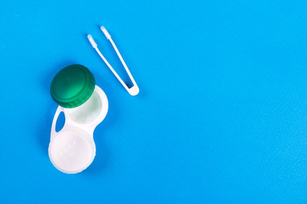 Container for contact lenses and tweezers on blue background