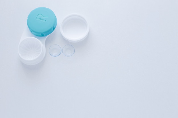 A container for lenses and two contact lenses lie on the side on a white background with space for t...