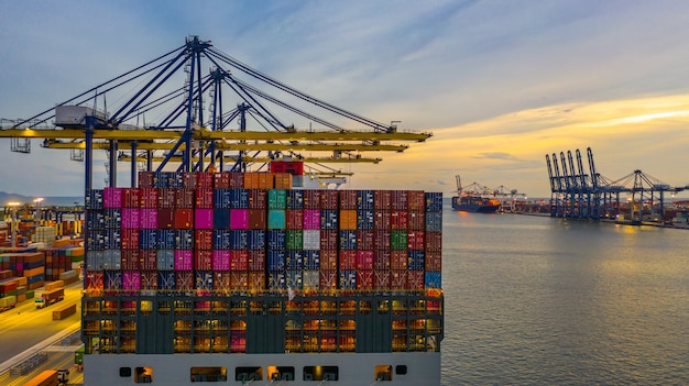 Nave porta-container che carica e che scarica nel porto marittimo profondo al tramonto, vista aerea dell'importazione e dell'esportazione logistiche di affari