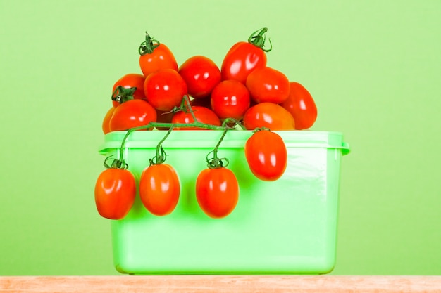 Container with fresh tomatoes on green background