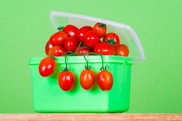 Container with fresh tomatoes on green background