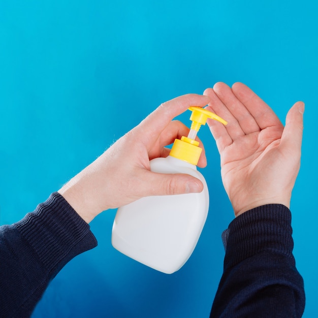 Container with liquid soap and hands on a blue background