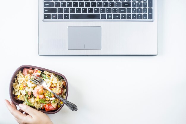 Photo container with salad with pasta in the workplace near the computer