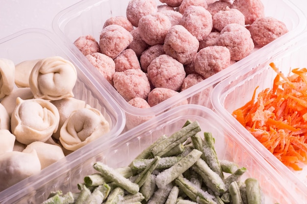 Containers with frozen  vegetables and semifinished meat products  from the refrigerator meatballs dumplings  chopped beans and grated carrots