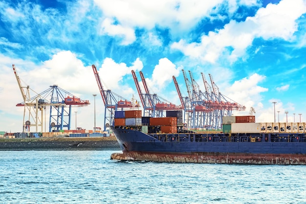 Containerschip in de vrachthaven van Hamburg aan de rivier de Elbe met kranen en containers. Containerterminal tegen blauwe hemel.