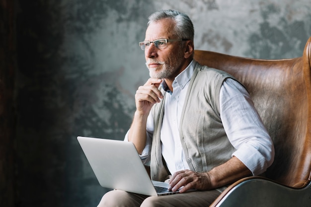 Photo contemplated elderly man sitting on chair with laptop against grunge background