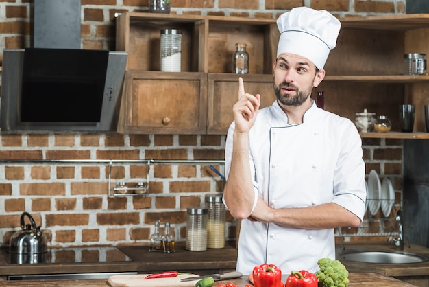 Foto contemplato chef maschio in cucina puntando il dito verso l'alto