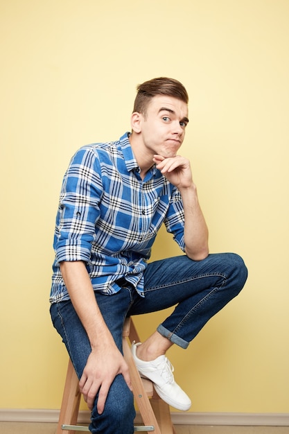 Contemplative guy is sitting on a stool on a yellow background in the studio .
