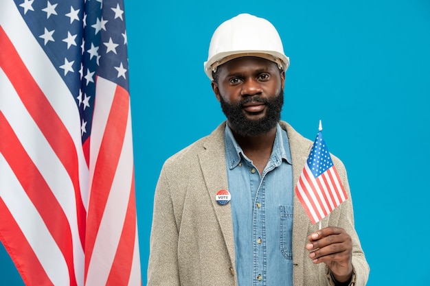 Contemporary African builder or engineer in helmet and formalwear holding small American flag