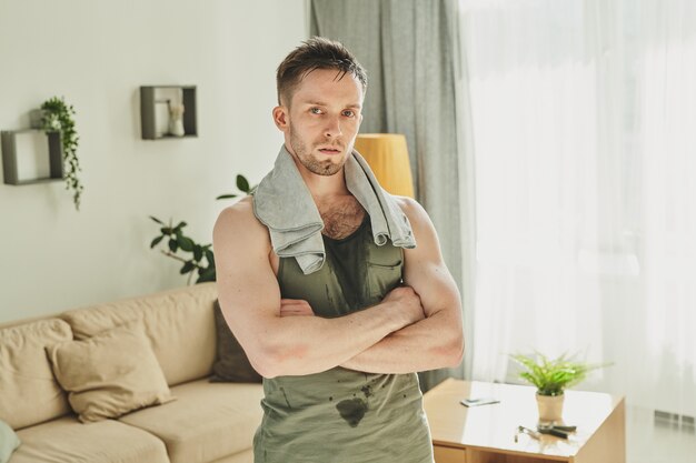 Contemporary athlete in sportswear with towel on neck crossing his arms by chest while standing in living-room after hard training